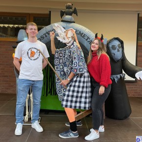 FSJ-ler Tom Weller im weißen Shirt und blauer Jeans, Schulleiterin Marion Marker-Schrotz als Hexe verkleidet und FSJ-lerin Kim Seibert mit Teufelshörnern vor einer Halloweendeko.