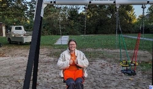 Eine Auszubildende mit orangefarbener Arbeitskleidung sitzt auf einer Schaukel
